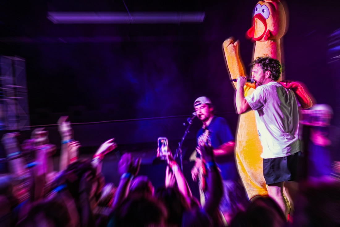 Singer on stage in front of a giant rubber chicken costume with the crowd cheering