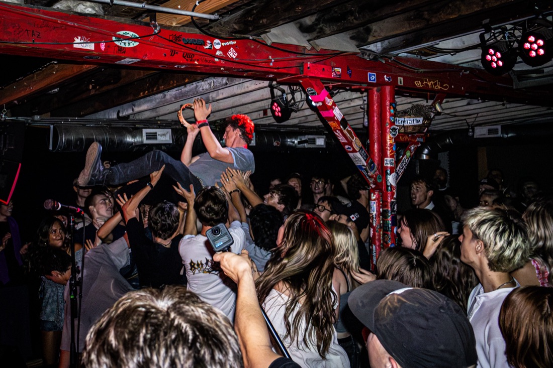 Singer crowd surfing with a tambourine in a packed basement venue