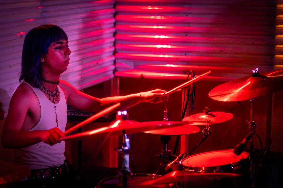 Drummer mid-hit under red stage lights