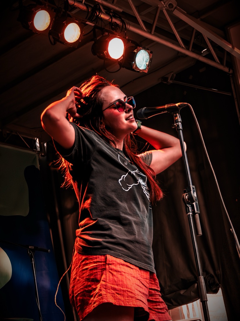 Singer in sunglasses with hands in her hair under stage lights
